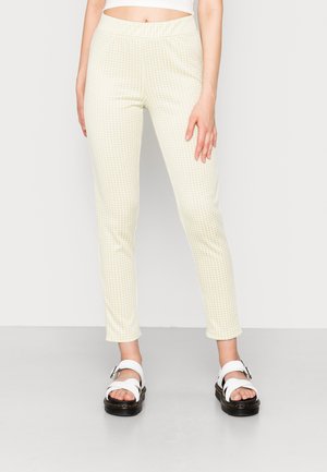 Leggings amarelos e brancos com padrão xadrez, cintura elástica, ajuste slim e textura suave, combinados com sandálias brancas chunky.