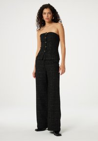 Zwarte strapless top met een gestructureerde afwerking, voorzien van gouden knopen aan de voorkant. Gecombineerd met zwarte wijde broek, beide in een vergelijkbare stof.