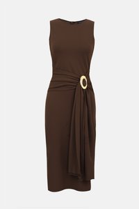 Robe marron sans manches, longueur genou, avec une ceinture drapée à la taille, attachée par une grande boucle circulaire dorée sur un fond uni.