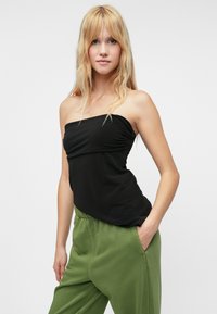 Black strapless top with gathered detail at the front, paired with loose green trousers. Smooth fabric, relaxed fit, and casual design.