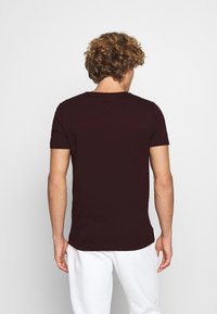 Burgundin värinen puuvillapaita lyhyillä hihoilla ja pyöreällä kaula-aukolla, esitetty takaa. Sujuva pinta yksinkertaisella designilla.
