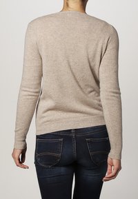 Beige stickad tröja med långa ärmar, ribbade muddar och fåll. Bärs med mörkblå jeans som har två bakfickor och kontrastsömmar.