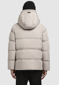 Helle beige Pufferjacke mit horizontalen gesteppten Abschnitten, angebrachter Kapuze und glatter Textur. Getragen mit einer schwarzen Strickmütze.