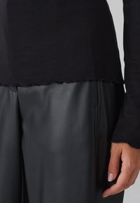 Schwarzes geripptes Strickoberteil mit gewelltem Saum, kombiniert mit schwarzen Lederhosen. Das Outfit präsentiert eine glatte Textur und eine maßgeschneiderte Passform.