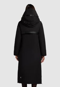 Black long puffer coat featuring a large hood, shiny finish, logo detailing on the back, and a sleek, modern silhouette.