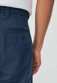 Navy trousers with herringbone texture, featuring a back pocket with a button, structured waistband, and smooth finish.