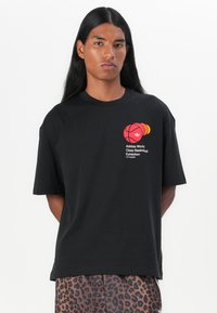 Svart bomulls-T-skjorte med et rødt og oransje basketballmotiv og logo. Korte ermer, avslappet passform, med trykt tekst under designet.