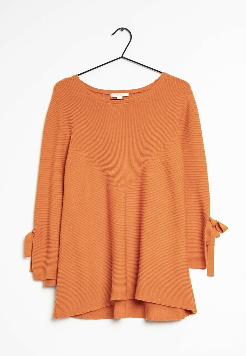 Haut à manches longues orange en maille côtelée avec encolure ronde et nœuds noués sur les manches, suspendu à un cintre noir sur un fond blanc.