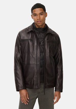 Brown leather jacket with a zippered front, two chest pockets, and a collar, layered over a black puffer jacket. Smooth texture, casual design.