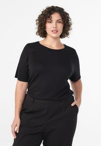 Melna īsroku blūze ar apaļu apkakli un gludu faktūru, kombinēta ar melnām piegrieztām biksēm. Vienkāršs dizains un neitrāla krāsa.