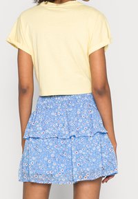 Żółta, skrócona koszulka z podwiniętymi rękawami, w połączeniu z niebieską, wielowarstwową spódnicą z kwiatowym wzorem w białe, czerwone i żółte akcenty.