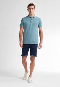 Jasnoniebieska koszulka polo z krótkimi rękawami, z prążkowanym kołnierzem; w zestawie z granatowymi szortami z podwiniętym mankietem oraz białymi trampkami. Prosty krój i wzór.