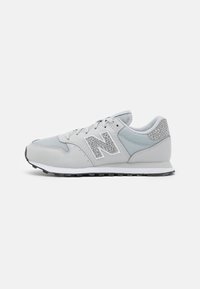 Light gray athletic shoe with mesh panels and leather accents. Features a white logo, textured gray detailing, and a rubber sole.