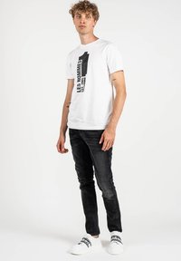 Camiseta blanca con un estampado gráfico negro, combinada con jeans ajustados negros y zapatillas blancas con detalles en negro.