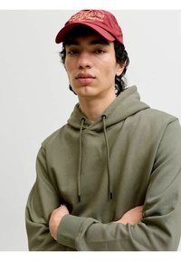 Felpa con cappuccio verde kaki con coulisse e polsini a coste, abbinata a un berretto color vinaccia con dettagli ricamati in oro del logo.