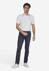 Weißes Poloshirt mit Kragen, marineblaue Slim-Fit-Jeans und weiße Sneaker; lässiges Outfit mit schlichtem Design und klaren Linien.