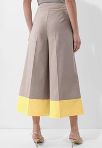 Lichte bruine wijde broek met een gele zoom. Gemaakt van katoen, met plooien en een hoog taille ontwerp. Soepele textuur met zijzakken.