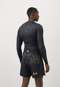 T-shirt de sport noir à manches longues avec logos dorés et motif serpent, associé à un short noir avec des lettres audacieuses et des accents.