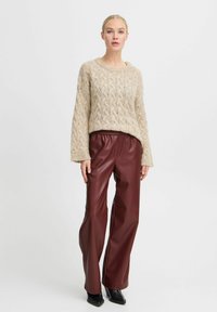 Beige kabelgebreide trui met brede mouwen, gecombineerd met hooggerokte, bordeaux faux leren broek. Zwarte hakken maken de look compleet.