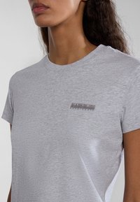Grijze katoenen T-shirt met korte mouwen, ronde hals en een klein, rechthoekig merklabel op de linkerkant van de borst. Zachte textuur.