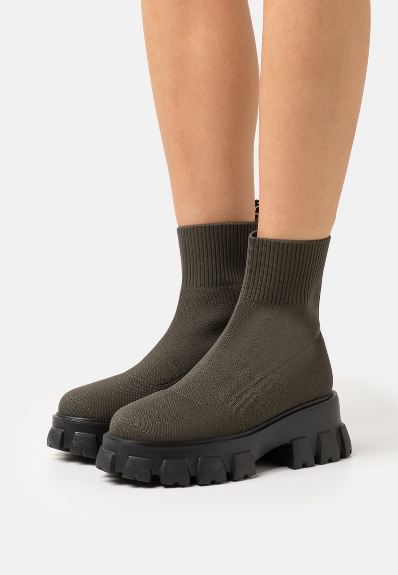 Bottes ankle vert foncé avec un bord côtelé, une forme épurée et une semelle noire épaisse avec des crampons en caoutchouc prononcés pour une meilleure adhérence.