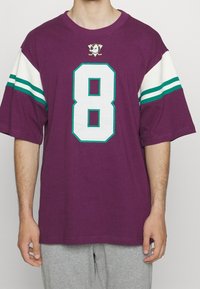 Camiseta morada de gran tamaño con mangas a rayas blancas y verdes agua, presenta un gran número 8 blanco y un logo en el pecho, fabricada en material de algodón.