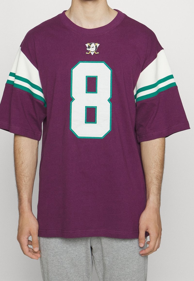 Camiseta morada de gran tamaño con mangas a rayas blancas y verdes agua, presenta un gran número 8 blanco y un logo en el pecho, fabricada en material de algodón.