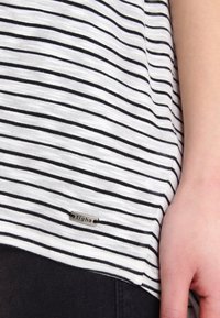 T-shirt a righe bianche e nere con maniche corte, caratterizzato da un piccolo etichetta metallica cucita nell'orlo. Tessuto morbido, vestibilità casual.