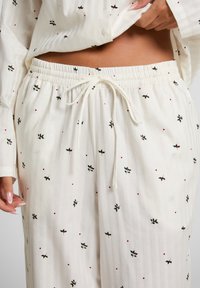 Crème-kleurige pyjama set met subtiele verticale strepen, voorzien van kleine patronen van rode en groene hulstbladeren, elastische tailleband met trekkoord.