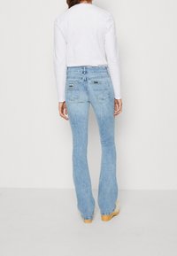 Vaaleansiniset, leveälahkeiset farkut, joissa on korkeavyötärö, hienovaraiset kulutukset ja logopatchi takataskussa.