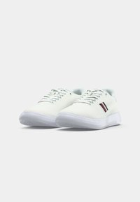 Witte sneakers met een gestructureerd oppervlak, voorzien van twee rode en zwarte strepen aan de zijkant, en een transparante rubberen zool. Standaard vetersluiting.