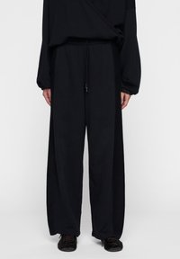Zwarte, wijde broek gemaakt van een zachte stof met een elastische tailleband en trekkoord. Heeft een gladde textuur en een comfortabele pasvorm.