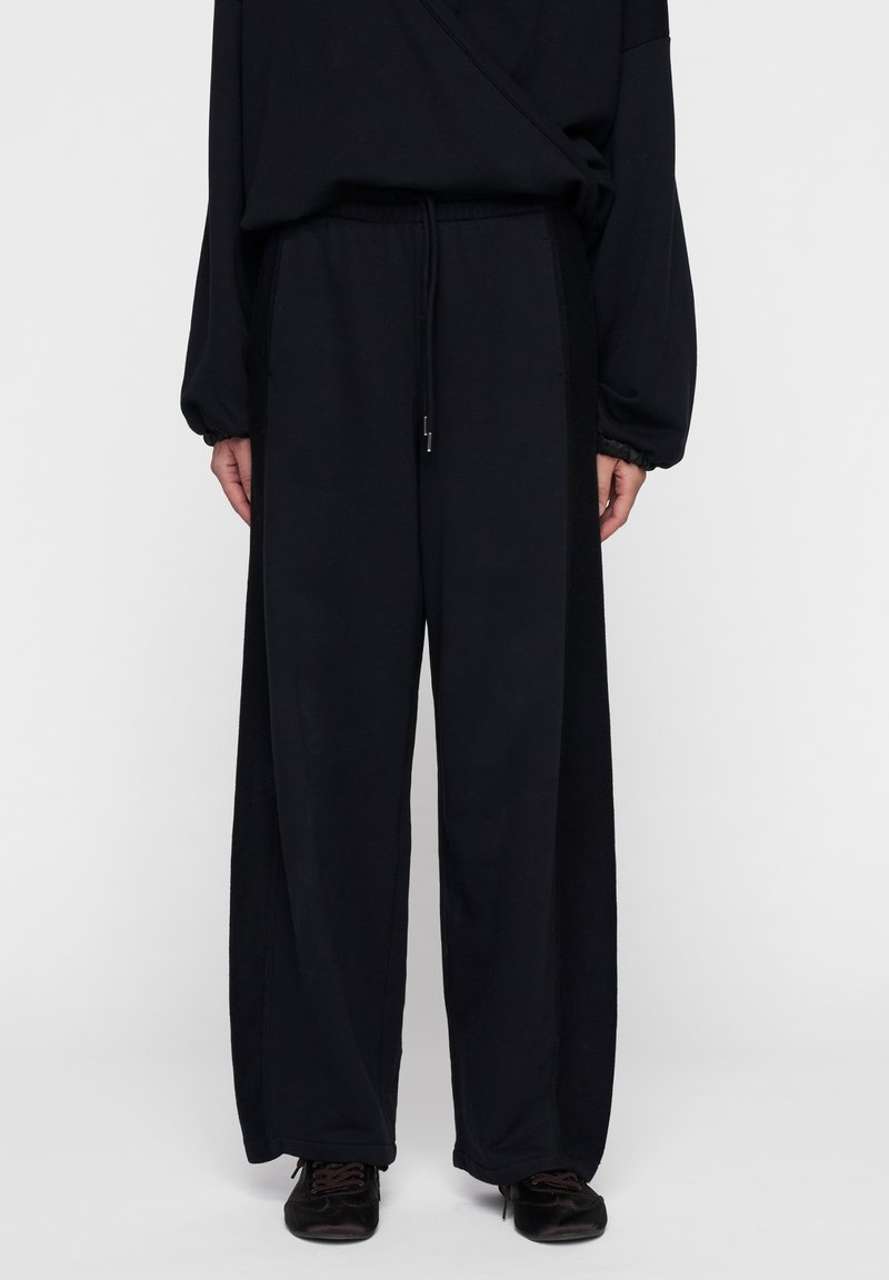 Zwarte, wijde broek gemaakt van een zachte stof met een elastische tailleband en trekkoord. Heeft een gladde textuur en een comfortabele pasvorm.