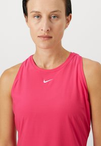 Ružový atletický top bez rukávov s okrúhlym výstrihom, s bielym logom Nike na hrudi. Hladká, ľahká látka.