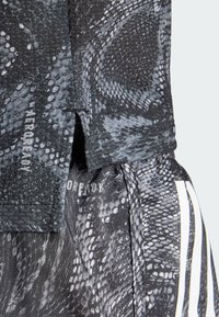 Černá a šedá sportovní tkanina se vzorem hadí kůže, s brandingem "AEROREADY" a kontrastními bílými pruhy. Texturovaný povrch.