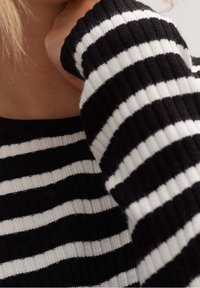 Maglione a righe bianche e nere in maglia, con texture a costine, righe larghe e scollatura quadrata, con manica parzialmente visibile.