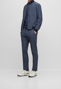 Mörkblå herrjacka med slim fit och tryckknappar, i kombination med matchande byxor och vita sneakers. Slät textur, minimalistisk design.