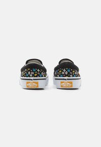 Chaussures noires à enfiler présentant un motif floral avec des fleurs multicolores. Semelle en caoutchouc blanche avec un logo Vans orange sur le talon.