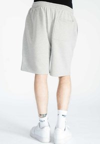 Pantaloni corti in cotone grigio chiaro con una vita elastica, dotati di due tasche laterali, che arrivano a metà coscia. Indossati con sneakers bianche e calze.