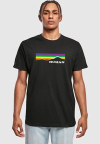 Black cotton t-shirt featuring a colorful rainbow wave graphic with the word "HUMAN" below, set against a light gray background.