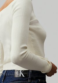 Off-white geribbelde lange mouwen top met een wijde hals, gecombineerd met donkerblauwe jeans met een zwart Calvin Klein Jeans label.