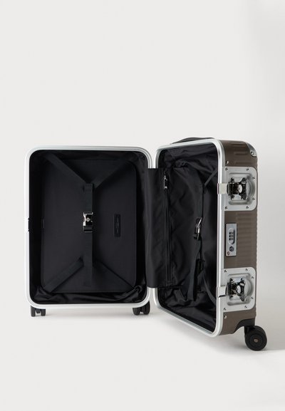 Valise rigide ouverte avec intérieur noir, sangles réglables, compartiments zippés, serrure à combinaison et quatre roulettes sur fond blanc.