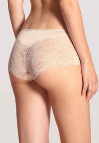 Lichtbeige kanten brazilian slip met ingewikkelde bloemenpatronen langs de randen en een gladde, transparante textuur aan de achterkant en zijkanten.