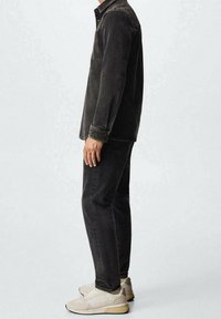 Chaqueta de mezclilla negra con un bolsillo en el pecho, combinada con vaqueros negros y zapatillas de deporte gris claro. El conjunto presenta un diseño minimalista y líneas limpias.