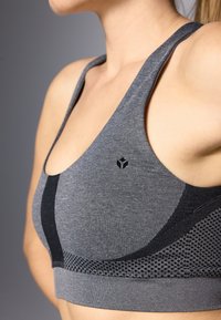Sostenedor deportivo gris con un diseño de espalda de nadador, que presenta un tejido texturizado, acentos negros y un logo sutil. Material suave y elástico.