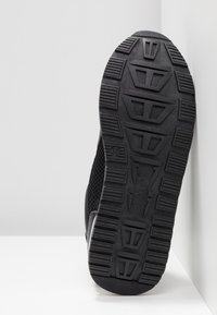 Czarne buty sportowe z teksturowaną gumową podeszwą, posiadające wyraźny geometryczny wzór bieżnika oraz siateczkowy design w górnej części dla lepszej wentylacji.