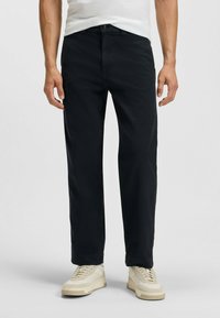 Svarta bomullsbukser med rak bendesign, med framknappslås och sidofickor, i kombination med ljusfärgade sneakers.