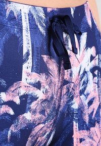 Navy swim shorts with a pink palm tree print, featuring a drawstring waistband and smooth fabric texture. Close-up view of the design.
