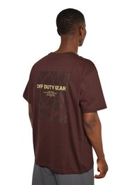 Man met kort haar draagt een bruine T-shirt met de tekst "OFF DUTY GEAR" en een abstract patroon op de achterkant, staand tegen een witte achtergrond.