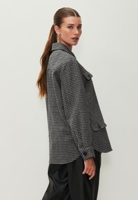 Giacca pied de poule bianca e nera con colletto, tasca frontale e maniche con bottoni, abbinata a pantaloni neri in similpelle.